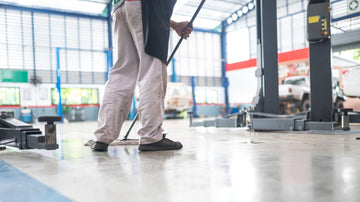 Janitor using a microfiber flat mop and commercial mop bucket in a facility hallway with various floor types