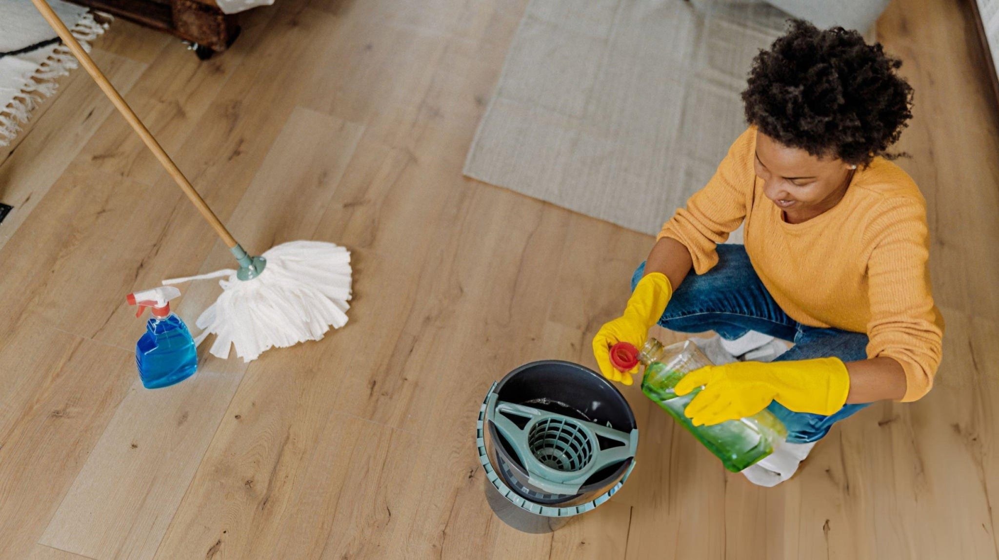 Natural floor cleaner ingredients including vinegar, baking soda and essential oils arranged beside spray bottle for DIY cleaning solutions