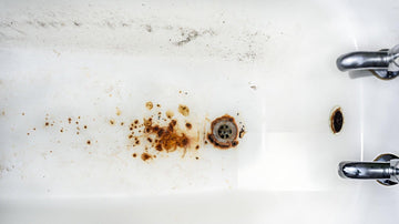 A clean bathroom with a white bathtub, rust stains being cleaned by a gloved hand using a spray bottle, demonstrating rust removal techniques.